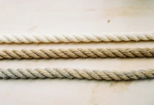 Trois cordes torsadées parallèles sur un plan de bois clair : coton écru, jute doré et chanvre beige grisé